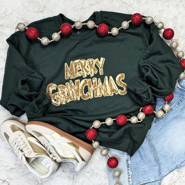 Merry GMas Gold Sequins Patch, holiday-themed black sweatshirt with gold glitter "MERRY GMas" text, decorated with red and silver Christmas ornaments and paired with white and gold sneakers and blue jeans.