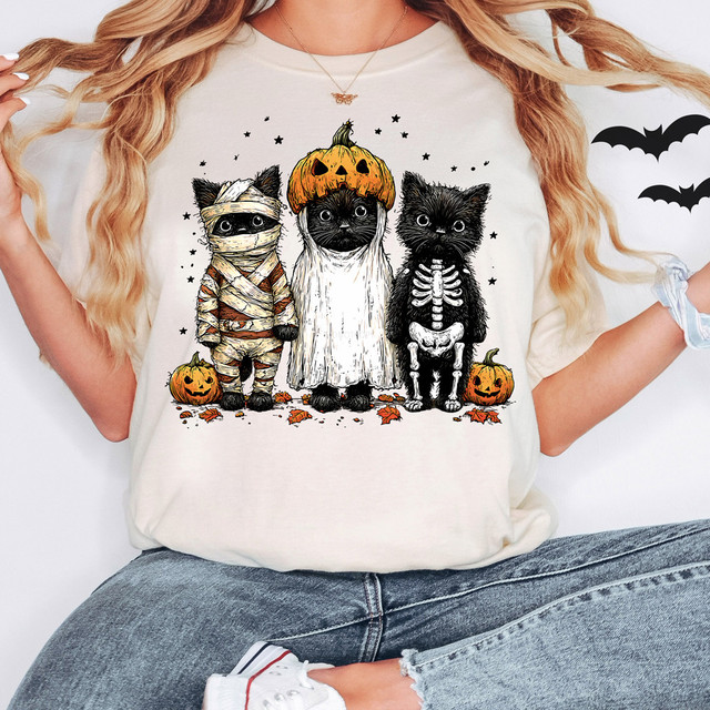 Halloween Black Cats DTF Heat Transfer, image of a woman wearing a Halloween-themed T-shirt featuring three cute black cats dressed in costumes with pumpkins and Halloween decorations.