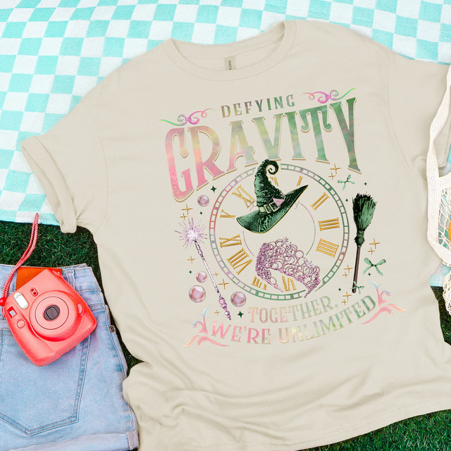 Defying Gravity Clock DTF Heat Transfer, colorful graphic T-shirt with magic hat, broom, and clock design, showcasing a creative and whimsical Halloween-themed artwork.