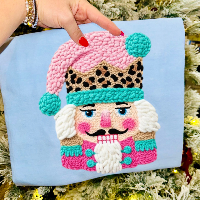 Faux Yarn Leopard Nutcracker DTF Heat Transfer, colorful plush velvet textured image of a Nutcracker with a pink hat, turquoise accents, leopard pattern, and a white beard on a blue background.