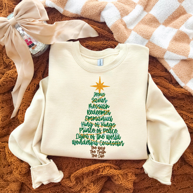 Jesus Name Tree DTF Heat Transfer, Christmas tree design with Christian words and phrases in green and brown colors displayed on a cream sweatshirt.
