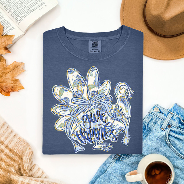 Give Thanks Painted Blue Floral Turkey DTF Heat Transfer, a decorative design on a blue T-shirt featuring a floral turkey with the words 'Give Thanks' in bold script.