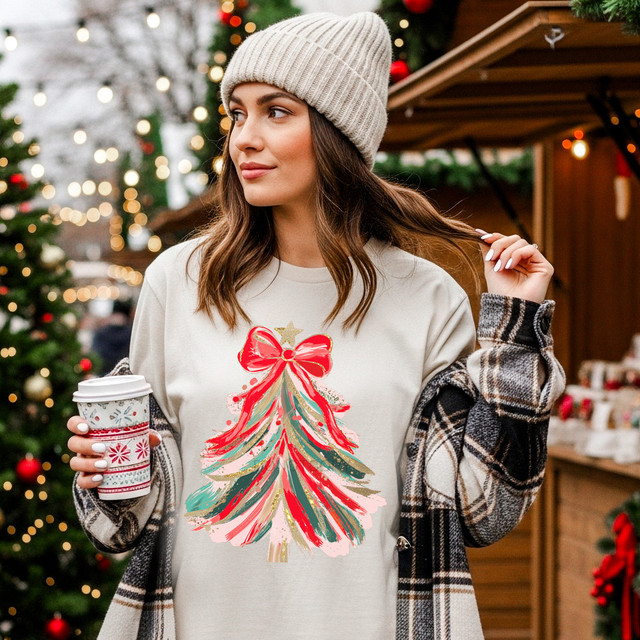 Brushstroke Tree With Star DTF Heat Transfer, Christmas-themed tree design with vibrant brushstroke colors and a star on top applied on a woman's cream T-shirt at a festive outdoor market.