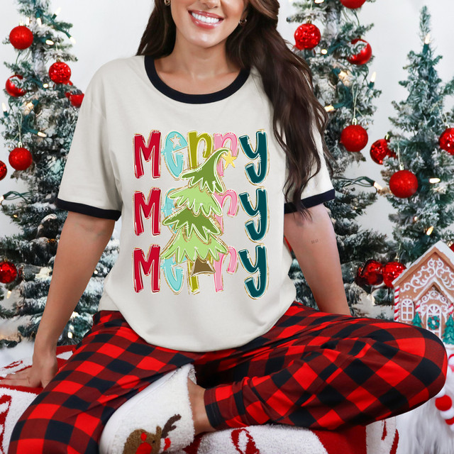 Stacked Merry Tree DTF Heat Transfer with colorful Christmas tree and 'Merry' text, applied on a white T-shirt worn by a smiling woman in front of Christmas trees.