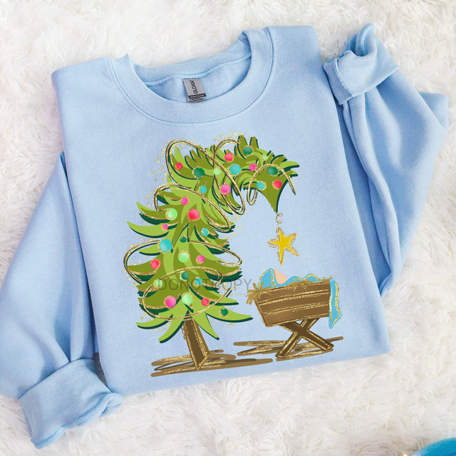 Leaning Tree & Manger DTF Heat Transfer, Christmas-themed fabric design featuring a decorated leaning tree and manger scene on a light blue shirt.