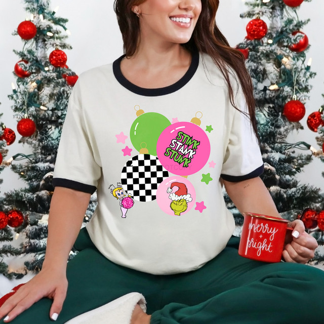 Green Guy Ornaments DTF Heat Transfer, colorful Christmas ornaments and holiday-themed characters on a woman wearing a festive shirt.