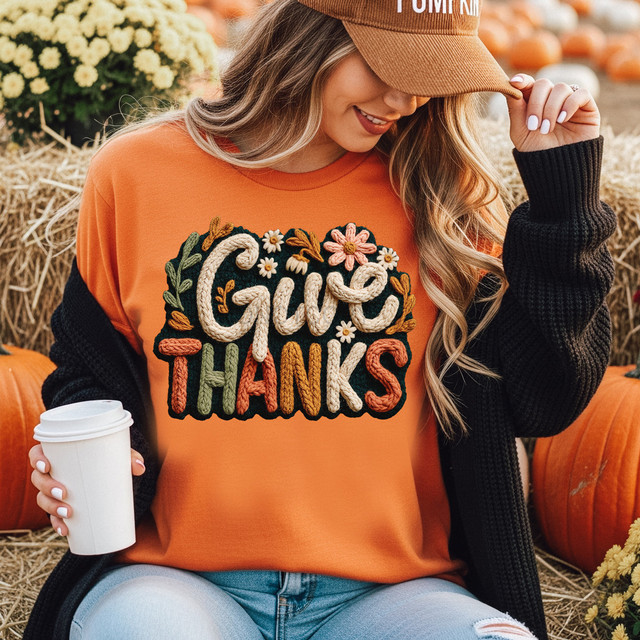 Faux Yarn Give Thanks Fall DTF Heat Transfer, embroidery design on an orange sweatshirt with fall leaves and flowers in a pumpkin patch setting.