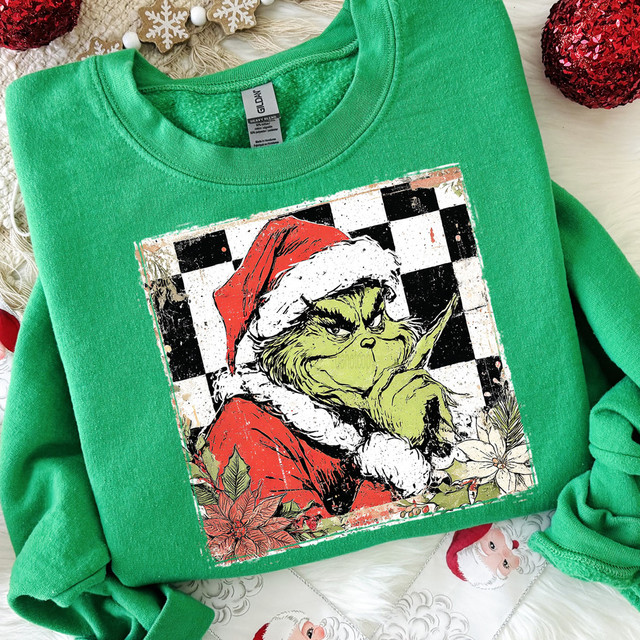 Distressed Checker Green Guy DTF Heat Transfer on a green sweatshirt featuring the Grinch dressed as Santa Claus with a mischievous expression, detailed floral accents, and a festive holiday theme.