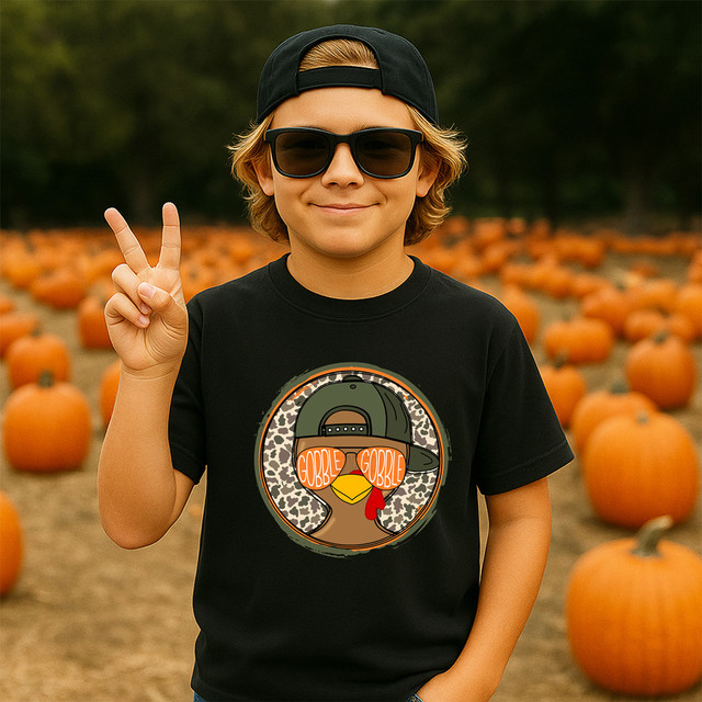 Gobble Glasses Snapback Turkey DTF Heat Transfer, a young boy wearing a black T-shirt with the turkey graphic, in a pumpkin patch.