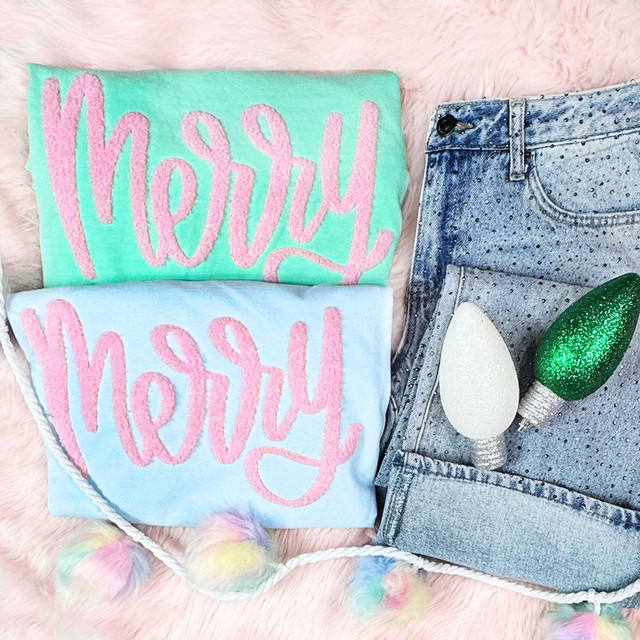 Mint and light blue folded shirts styled with fluffy pink “Merry” chenille-style patches, holiday lights, and denim shorts.