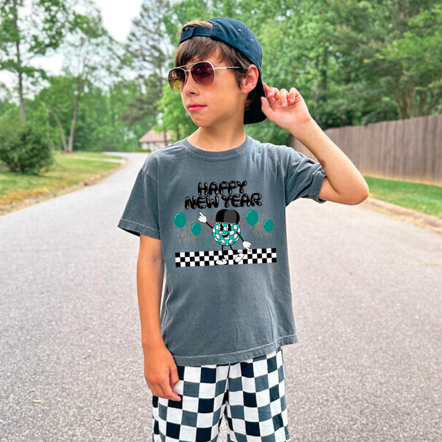 Retro Happy New Year Snapback DTF Heat Transfer, a boy wearing a gray T-shirt with a festive design and checkered shorts, outdoors during daytime.