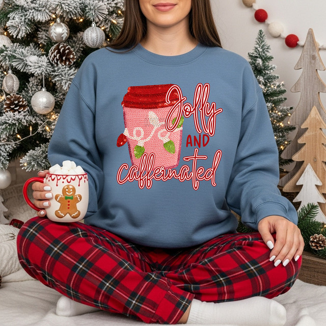 Faux Yarn Jolly & Caffeinated DTF Heat Transfer, Christmas-themed sweatshirt with a graphic of a coffee cup with a red lid and a gingerbread cookie mug, Christmas decorations in the background.