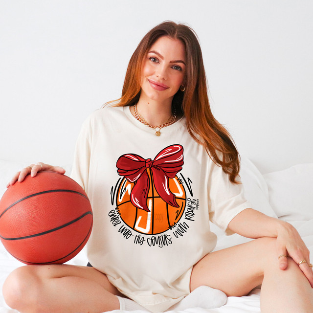 Enter His Courts With Praise Red DTF Heat Transfer - A woman in a white t-shirt with a basketball graphic and red bow, holding a basketball and smiling at the camera.