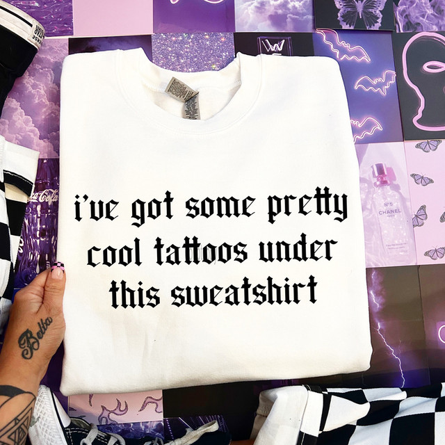 I've Got Some Pretty Cool Tattoos Under This Sweatshirt, white sweatshirt with black text indicating cool tattoos underneath.