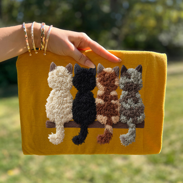 Faux Yarn Mixed Cats DTF Heat Transfer, a decorative textile art piece featuring four plush, fuzzy cats in different colors sitting on a brown bench, with a yellow background and a blurred outdoor setting.