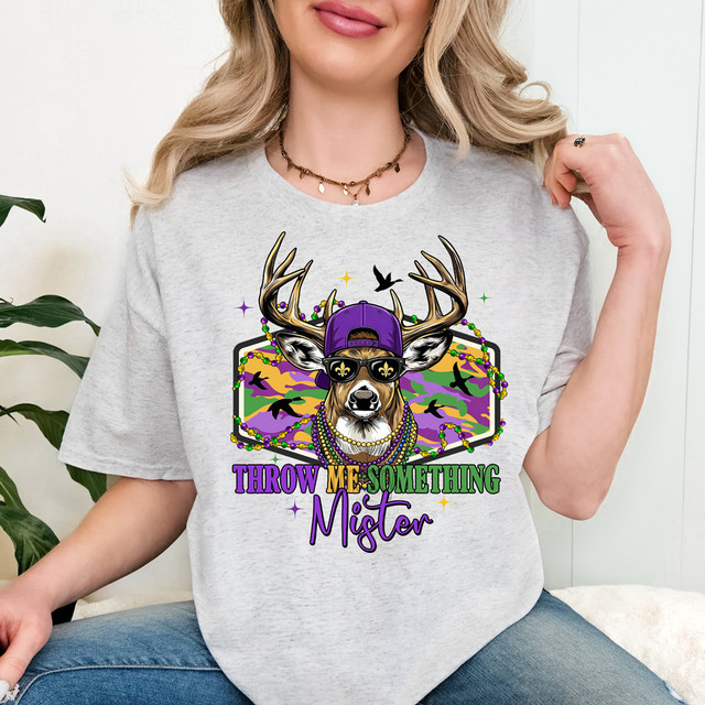 Throw Me Something Mister DTF Heat Transfer, colorful graphic design of a deer with sunglasses, beads, purple cap, and multiple silhouettes of birds in a camouflage background on a gray t-shirt.