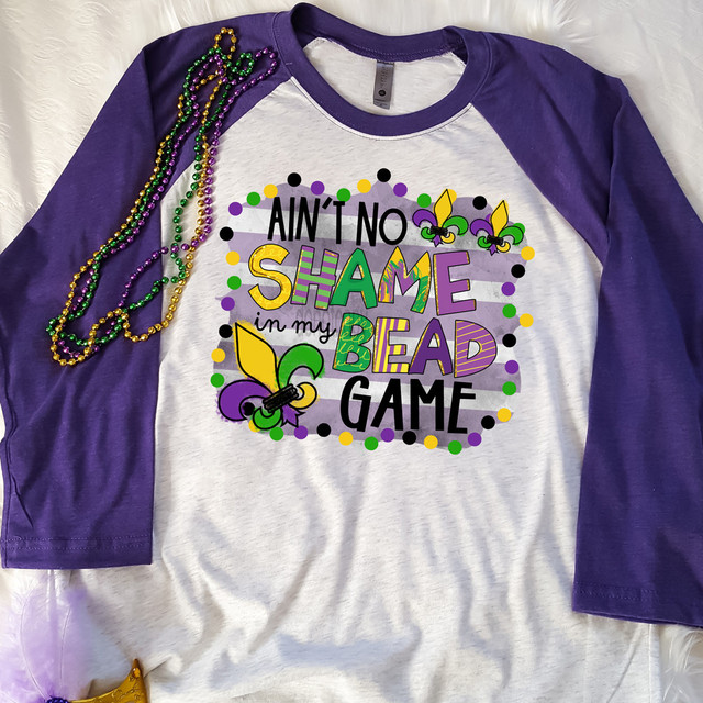 Ain't No Shame In My Bead Game DTF Heat Transfer, colorful Mardi Gras themed t-shirt with beads and decorative beads on the shoulder.