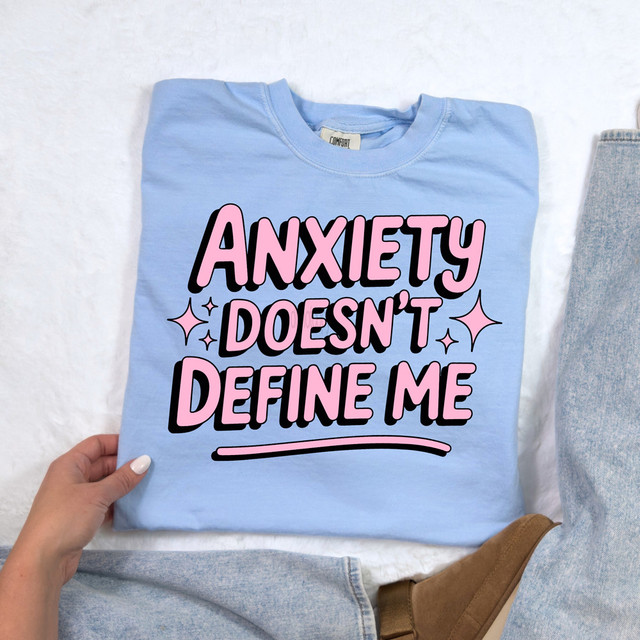 Product Anxiety Doesn't Define Me DTF Heat Transfer, pink lettering on light blue t-shirt with decorative stars.