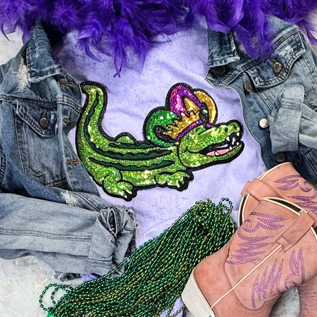 Mardi Gras Gator Sequins Patch, colorful sparkling green, purple, and yellow embroidered patch on a purple shirt, surrounded by denim jacket, pink cowboy boot, and green beads.