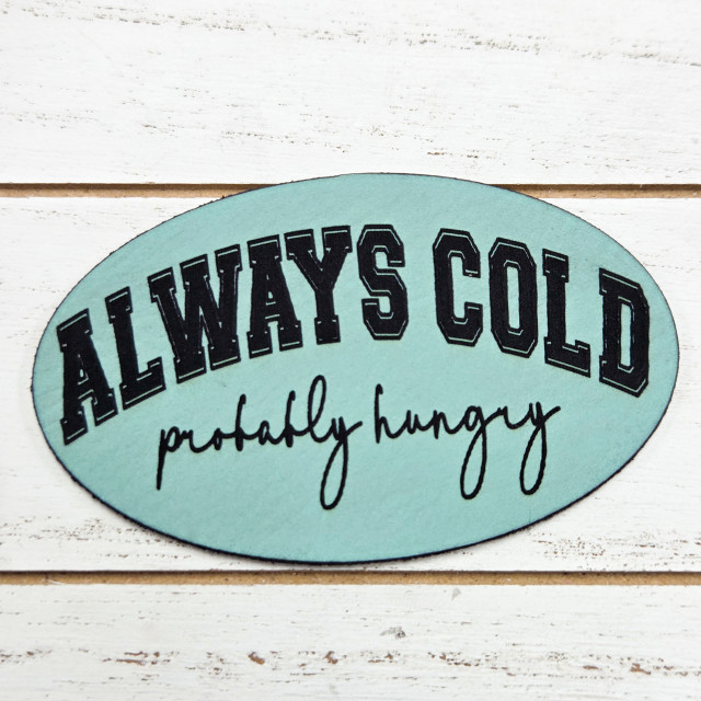 Always Cold Probably Hungry Faux Leather Patch, humorous clothing accessory with black text on a light blue background.