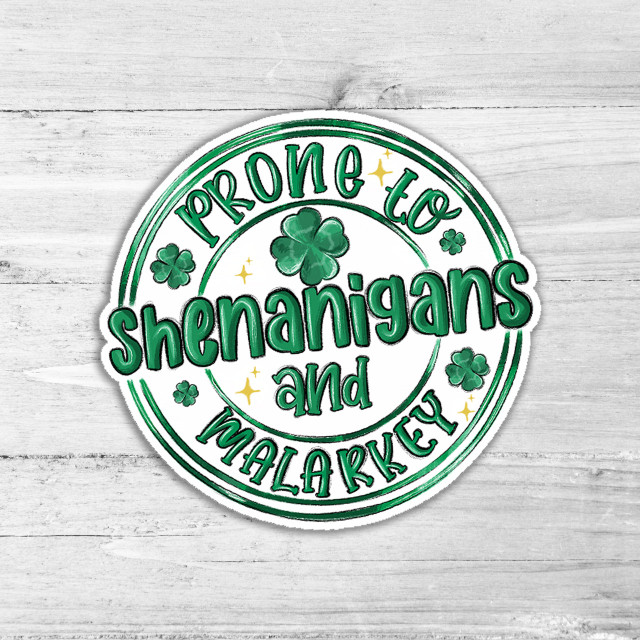 Prone To Shenanigans Die Cut Sticker, festive green shamrocks and gold stars with playful text on a white wooden background.