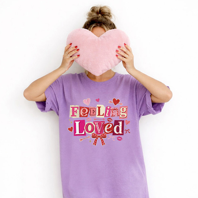 Retro Feeling Loved DTF Heat Transfer, a colorful graphic design on a purple T-shirt with hearts, bows, and the words Feeling Loved in a playful font.