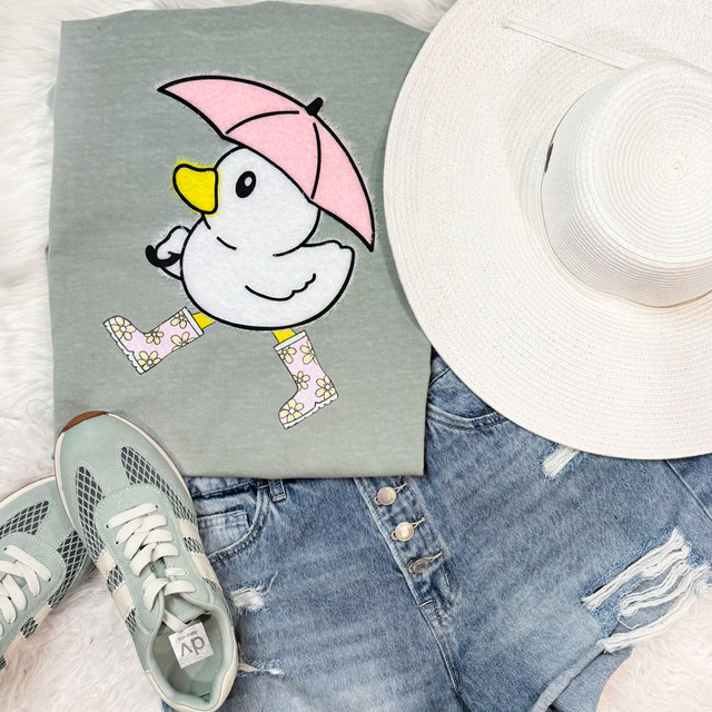 Spring Fluffy Duck Patch, cute cartoon duck wearing pink umbrella hat, rain boots, and yellow beak, embroidered on gray T-shirt.