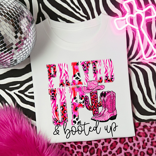 Prayed Up and Booted Up SET DTF Heat Transfer, image of a vibrant design with pink leopard print and cowboy boots on a white shirt, surrounded by pink animal print, zebra pattern fabric, a disco ball, and neon pink cowgirl hat light.