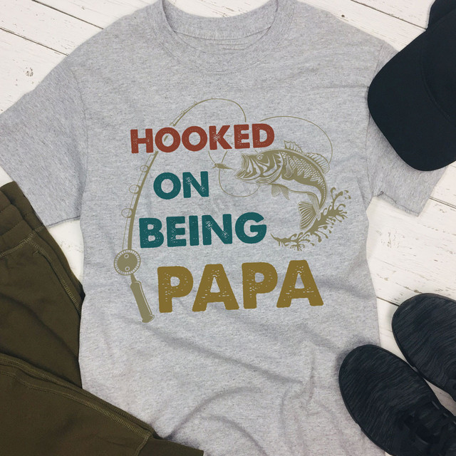 Hooked On Being Papa DTF Heat Transfer, graphic T-shirt with fishing-themed design and text.
