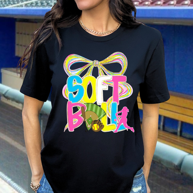 Softball Oversized Bow DTF Heat Transfer - Colorful design with a large bow and multiple sports-related icons on a black T-shirt worn by a woman outdoors.