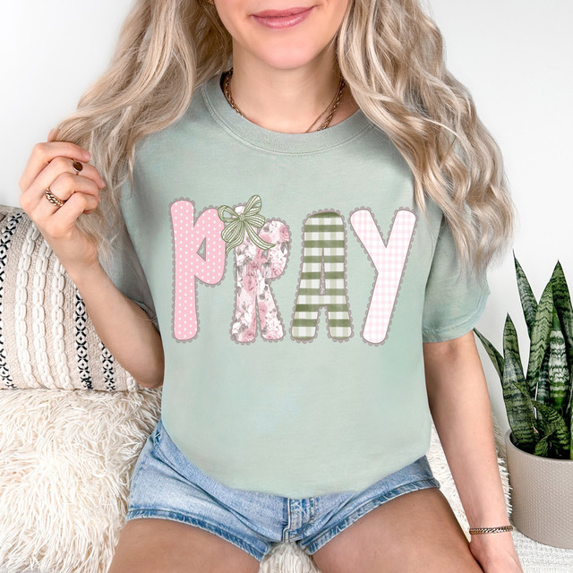 Pray Pink/Green Pattern DTF Heat Transfer, image of a woman wearing a pastel green t-shirt with a colorful, patterned prayer design.