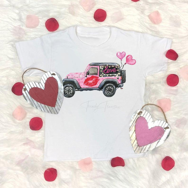 Love Jeep Valentines Jeep Sublimation Transfer, white T-shirt with pink Jeep design, hearts, and love-themed graphics surrounded by red and pink rose petals and heart-shaped ornaments.