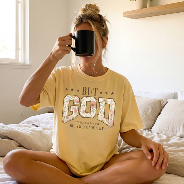 But God Boho DTF Heat Transfer, a woman drinking coffee in a cozy bedroom wearing a yellow T-shirt with floral print text.
