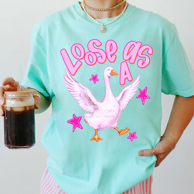 Loose As A Goose DTF Heat Transfer, A pink cartoon goose with spread wings on a light blue T-shirt with the phrase 'Loose As A' and pink stars.