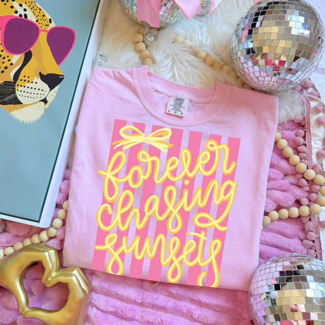 Forever Chasing Sunsets Stripes DTF Heat Transfer, pink t-shirt with yellow script and bow design, surrounded by disco balls, beaded necklace, and decorative items in a colorful, festive setting.