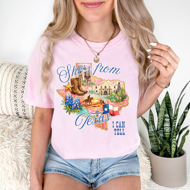 She's From Texas DTF Heat Transfer, colorful graphic design on pink t-shirt with Texas map, cowboy boots, cowboy hat, water tower, cactus, and Texas flag.