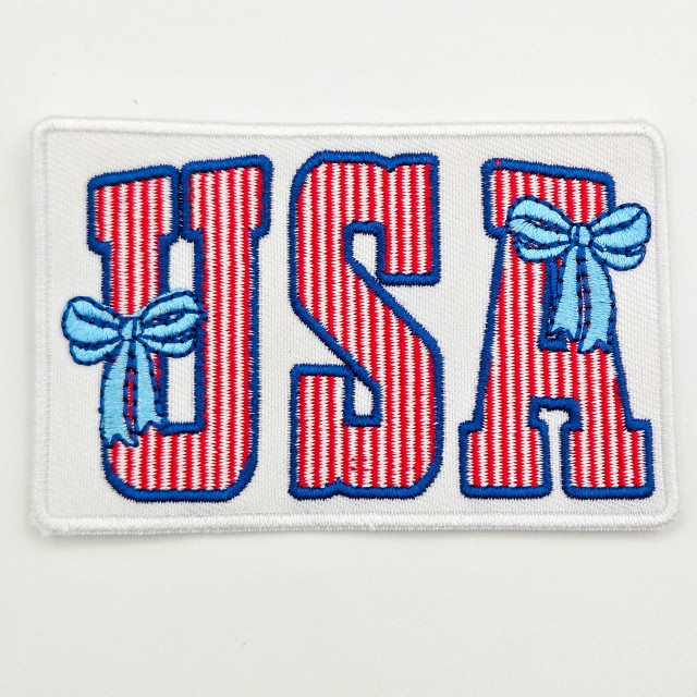 USA Coquette Embroidered Hat Patch – 3.5” Wide, embroidered patch with red and white striped letters 'USA' outlined in blue, featuring two light blue bows on the 'U' and 'A', designed to be sewn onto hats or clothing.