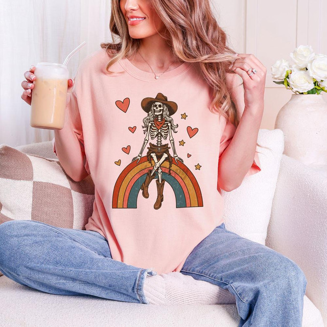 Cowgirl Skeleton Rainbow DTF Heat Transfer, colorful skeleton design on a pink T-shirt with rainbow, hearts, stars, and cowgirl hat features.
