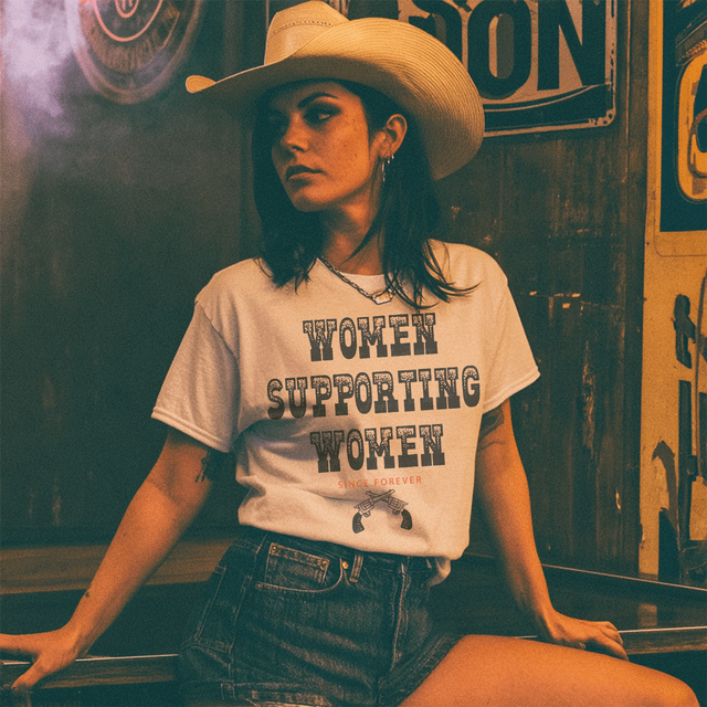 Women Supporting Women DTF Heat Transfer, a woman wearing a white T-shirt with the text 'Women Supporting Women Since Forever' printed on it, paired with a cowboy hat in a vintage-themed setting.