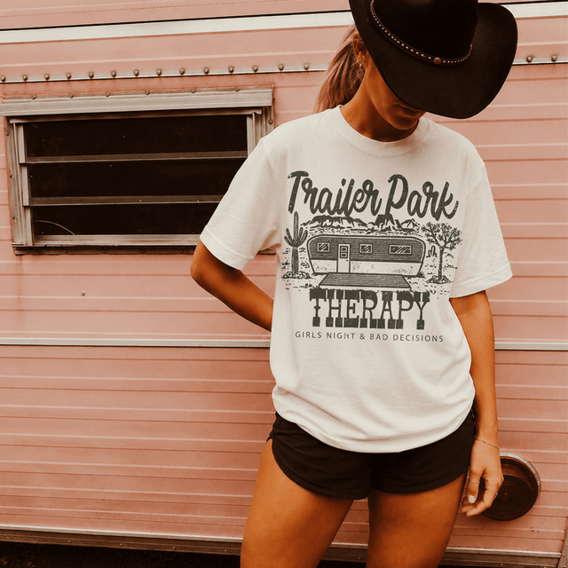 Trailer Park Therapy - Girls Night & Bad Decisions DTF Heat Transfer, a woman wearing a white t-shirt with a trailer park graphic and text, standing in front of a pink camper trailer.