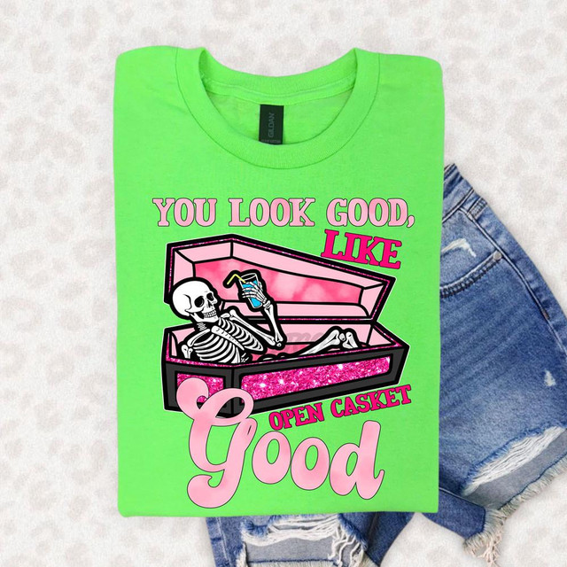 You Look Good Like Open Casket Good DTF Heat Transfer, bright green T-shirt with a skeleton graphic and pink glitter accents, featuring the phrase 'You Look Good, Like Open Casket Good' in bold text.