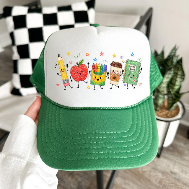School Doodles DTF Heat Transfer, colorful cartoon school supplies characters on white and green cap, including a pencil, apple, crayon box, coffee cup, and notebook.
