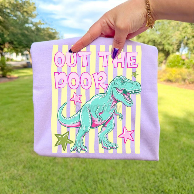 Out The Door Dinosaur DTF Heat Transfer, colorful dinosaur graphic on a purple fabric bag with vibrant text and star designs.