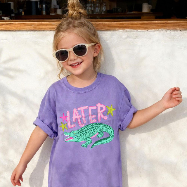 Later Gator DTF Heat Transfer, a colorful cartoon alligator and the word 'LATER' on a purple t-shirt worn by a little girl.