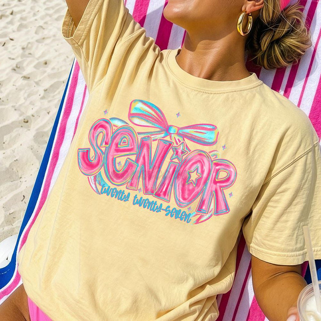 Senior Twenty Twenty-Seven Bow DTF Heat Transfer on a yellow t-shirt featuring vibrant pink, blue, and purple design with text and a bow graphic.