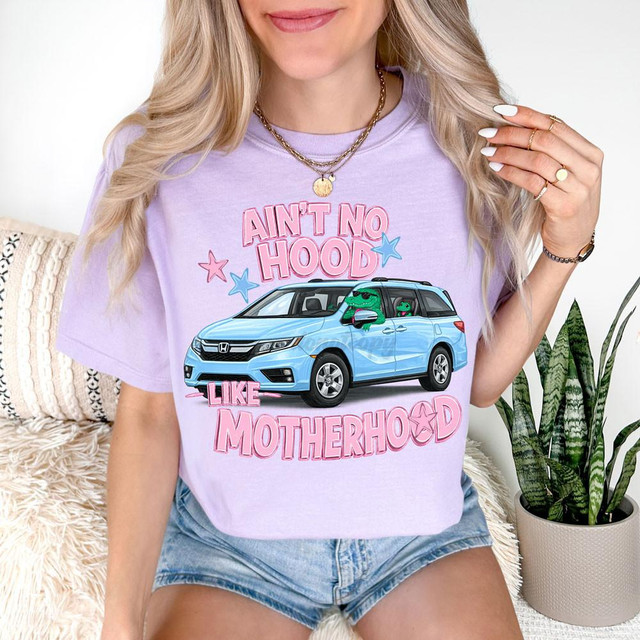 Ain't No Hood Like Motherhood Minivan DTF Heat Transfer, woman wearing a pastel purple t-shirt with a graphic of a blue minivan, and cartoon characters inside, with pink and blue stars around, celebrating motherhood.