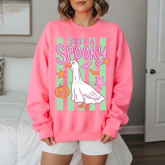Just A Spooky Goose DTF Heat Transfer, colorful Halloween-themed design featuring a cartoon goose with a pumpkin, stars, bats, and the text 'Just A Spooky' on a pink sweatshirt.