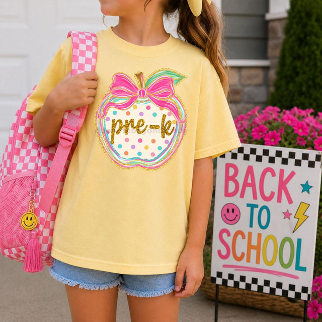 Polka Dot Grade Apple DTF Heat Transfer, colorful polka dot design with pink bow and gold 'pre-k' lettering on a yellow t-shirt worn by a girl carrying a pink checkered backpack.