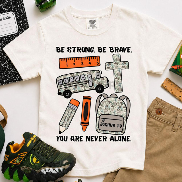 Be Strong, Be Brave, You Are Never Alone Joshua 1:9 DTF Heat Transfer T-shirt with religious and motivational design featuring a camo pattern ruler, bus, cross, backpack, and markers.