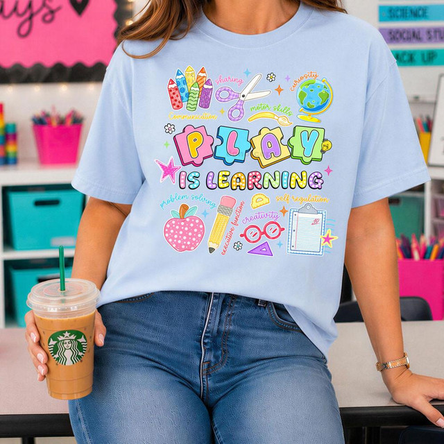 Play Is Learning DTF Heat Transfer, colorful educational design with illustrations of pencils, scissors, globe, apple, and school supplies on a girl's light blue t-shirt.